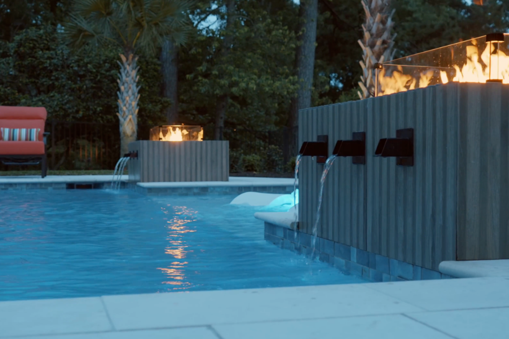 Elegant pool design with water features and fire elements, bordered by palm trees. Ideal by a custom pool builder for a luxurious backyard.