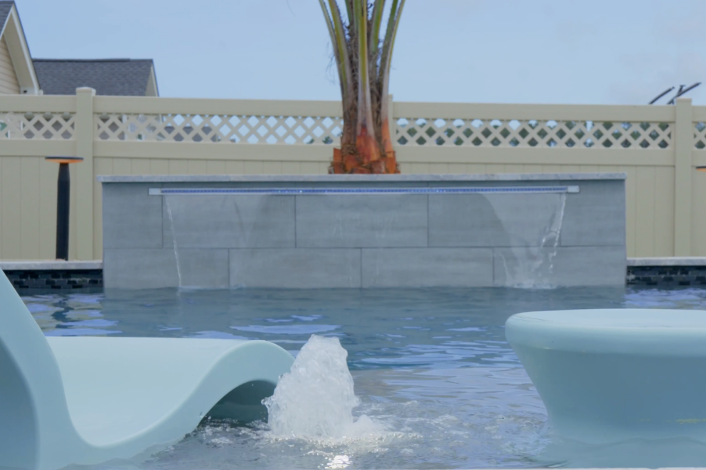 Modern pool with water jets, lounge chairs, and palm tree backdrop, showcasing the work of a custom pool builder.