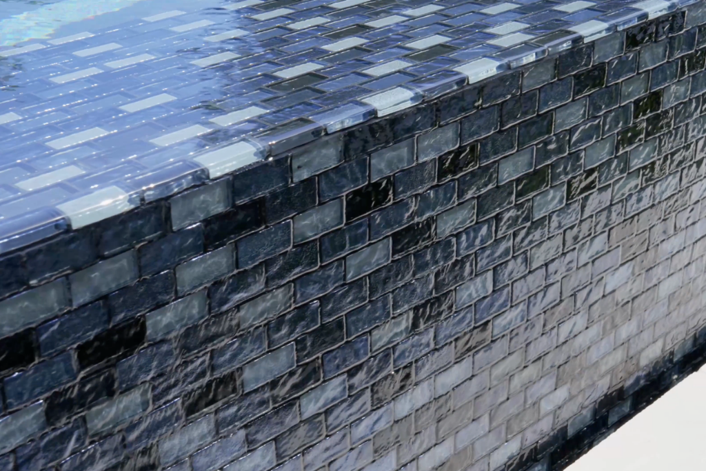 Reflective glass tiles on a custom pool edge by a custom pool builder, creating a shimmering water effect.