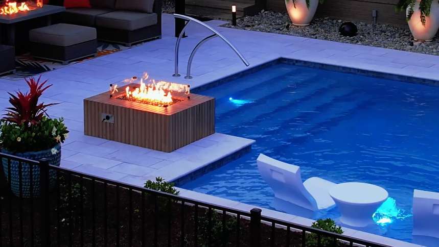 Luxurious backyard with a modern custom pool featuring submerged seating and a nearby fire pit, surrounded by elegant patio furniture.