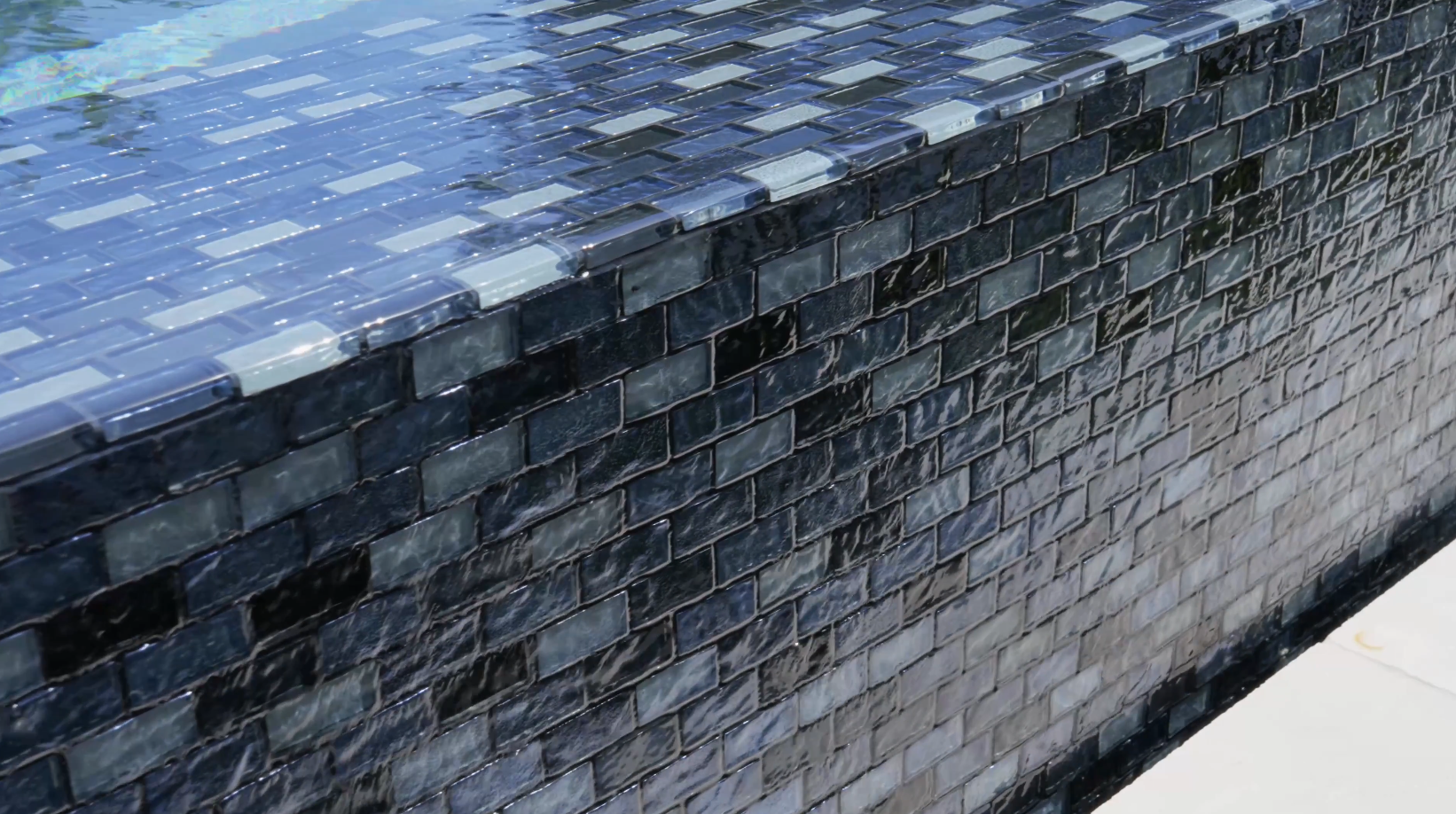 Glazed ceramic tiles in varying blue shades create a sleek infinity pool edge, crafted by a custom pool builder.